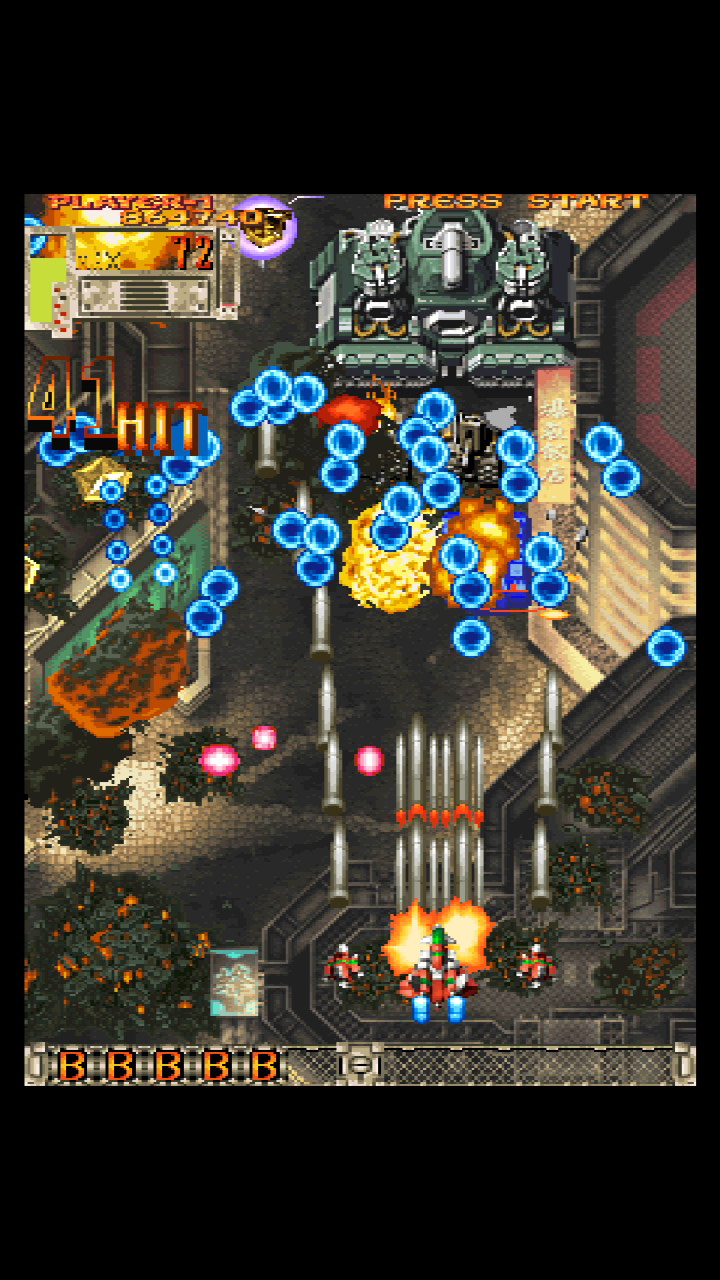 A screenshot from the game DoDonPachi DaiOuJou, with the player fighter-craft firing a large volley of projectiles at an enemy tank while dodging a complex bullet pattern.